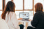 Two women look at a laptop computer on a white table
