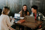 Three people sitting around a table with computers and laughing