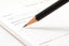 A black pencil writing on a white notepad