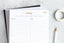 An organizing pad, a planner, and a pencil on a marble tabletop.