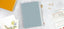 A light blue planner on a white desk with an array of paper accessories.
