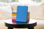 A stack of colorful planners on a dark wood table in front of a white couch