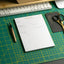 Notepad with an action plan on a green cutting mat with a keyboard and scissors in the background.