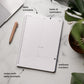 Planner with sections labeled for daily schedule, tasks & reminders, wellness trackers, and notes with daily prompts on a marble surface.