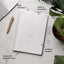 Planner with sections labeled for daily schedule, tasks & reminders, wellness trackers, and notes with daily prompts on a marble surface.